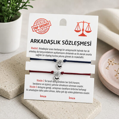 Beyaz dekoratif taş üzerinde sergilenen arkadaşlık sözleşmesi kartı ve gümüş kalpli 2'li ip bileklik
