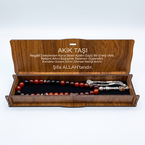 Kapağında akik taşının faydaları yazılı olan ahşap hediye kutusu içinde siyah sünger üzerinde yatan akik tesbih.